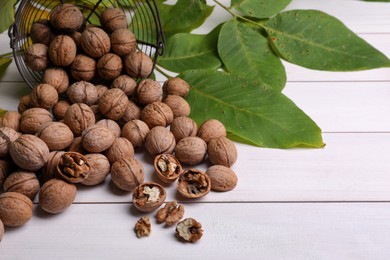 Pile of ripe walnuts and fresh leaves on white wooden table