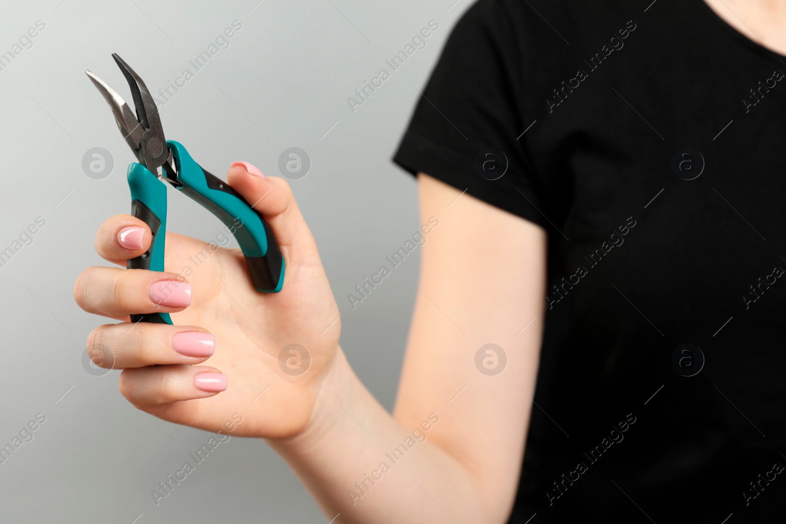 Photo of Woman with bent nose pliers on grey background, closeup. Space for text