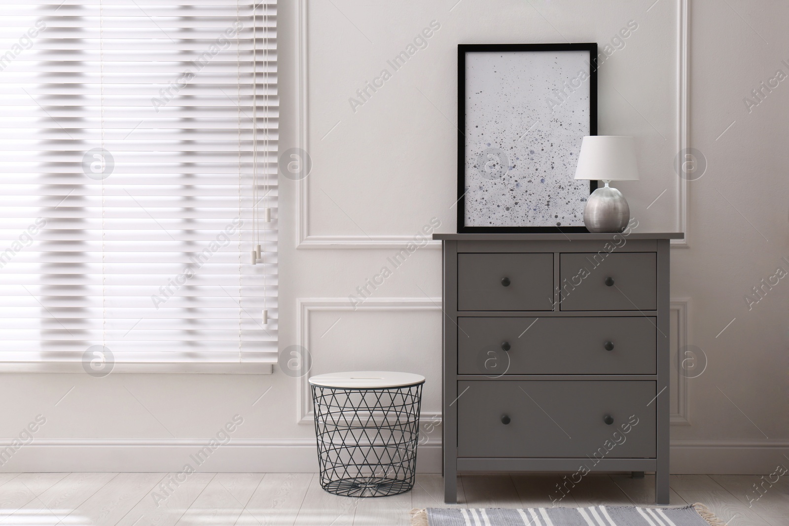 Photo of Grey wooden chest of drawers with lamp and picture near white wall in room, space for text. Interior design