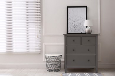Photo of Grey wooden chest of drawers with lamp and picture near white wall in room, space for text. Interior design
