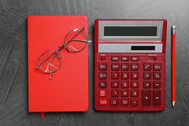 Photo of Calculator, glasses and notebook on dark grey background, flat lay. Tax accounting