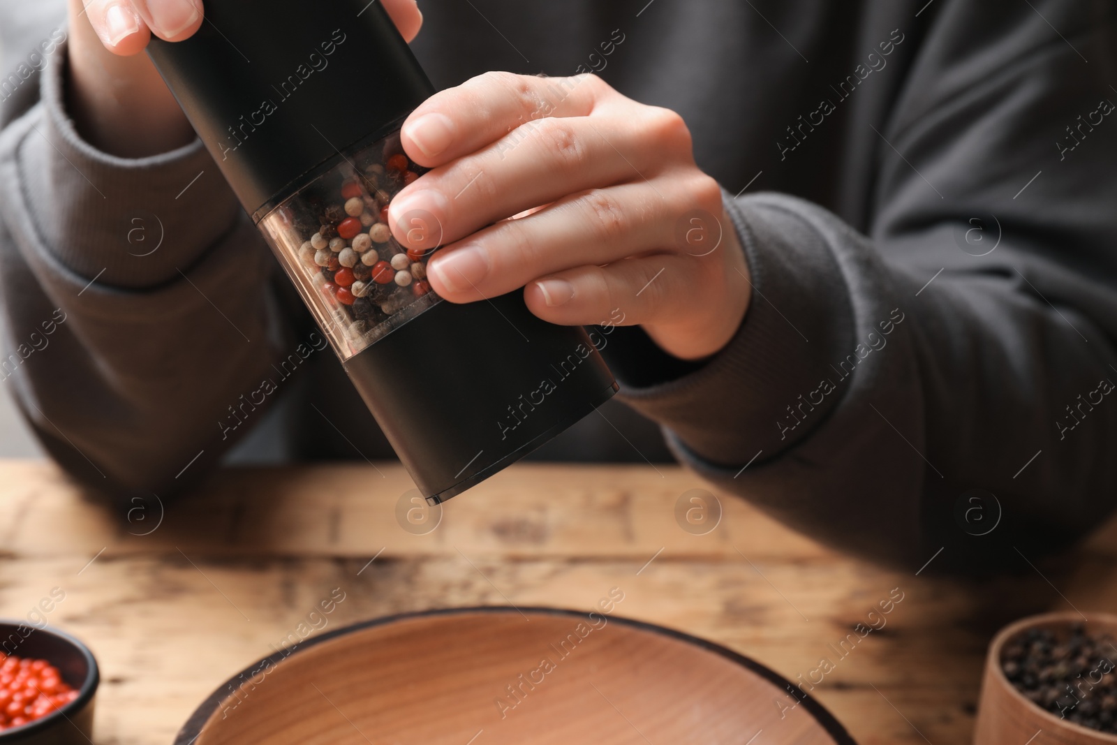 Photo of Woman grinding pepper with shaker at wooden table, closeup