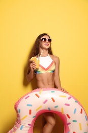 Photo of Beautiful young woman with inflatable ring and glass of cocktail on color background