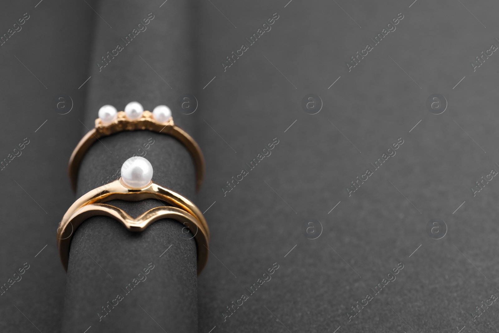 Photo of Elegant pearl rings on black background, closeup. Space for text