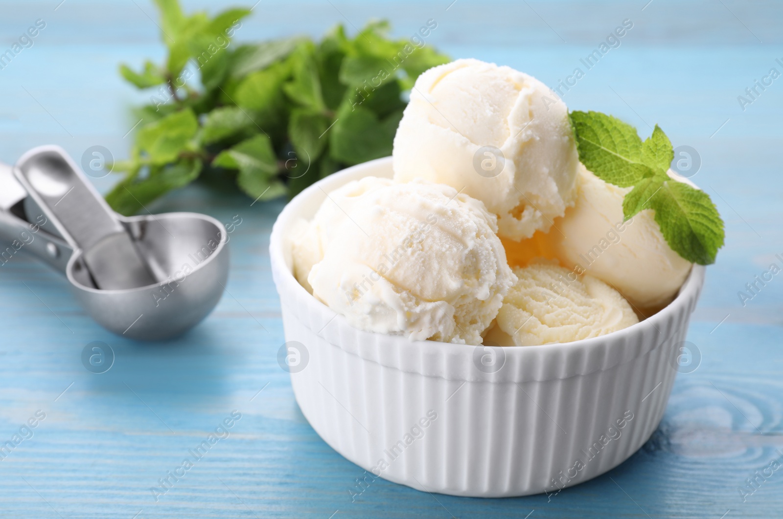 Photo of Delicious vanilla ice cream with mint on light blue wooden table, closeup. Space for text