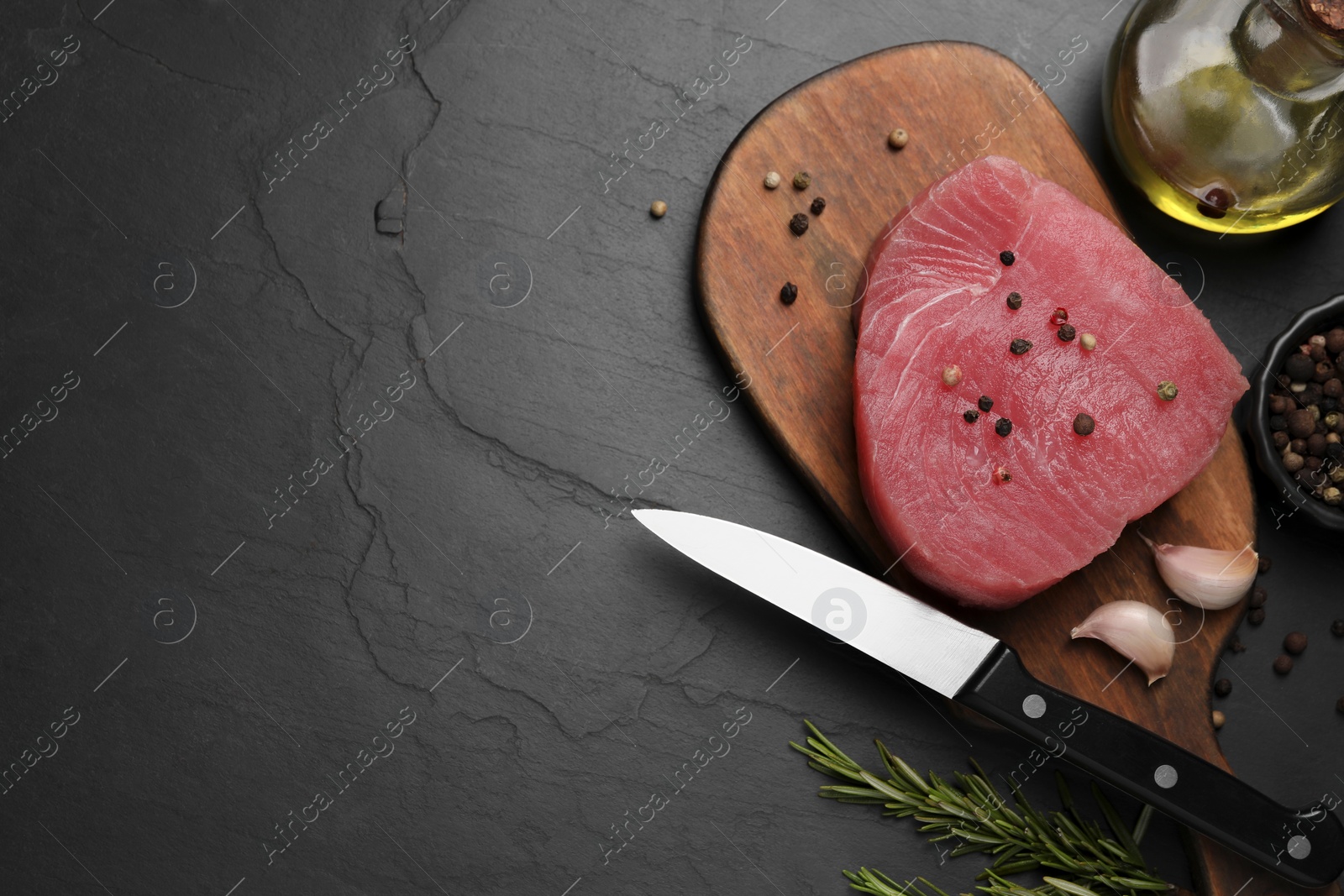 Photo of Raw tuna fillet, spices and oil on black table, flat lay. Space for text