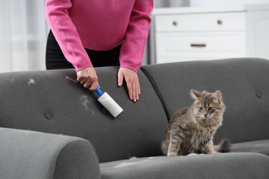 Photo of Pet shedding. Woman with lint roller removing cat`s hair from sofa at home, closeup