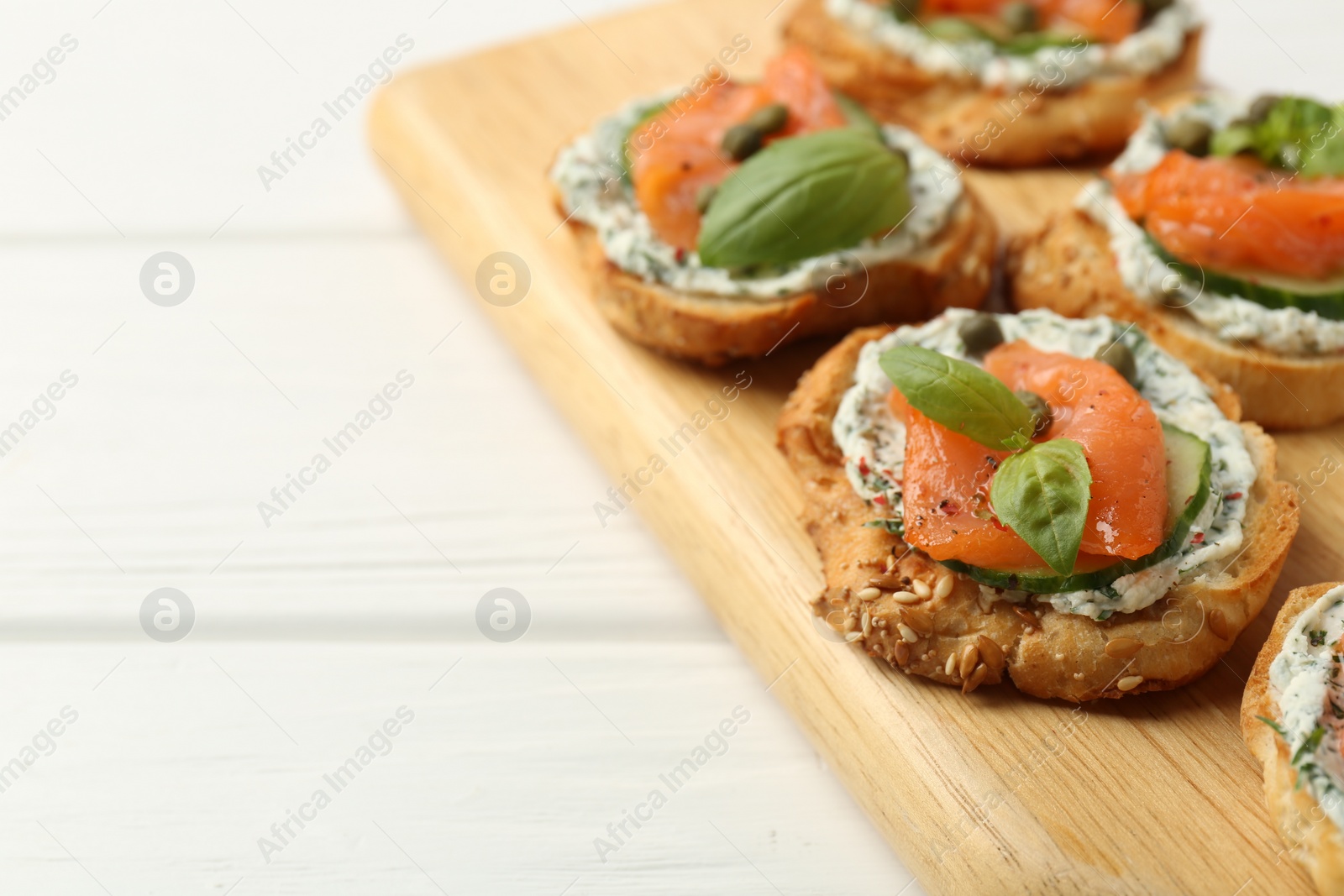 Photo of Tasty canapes with salmon, capers, cucumber and sauce on white wooden table, closeup. Space for text