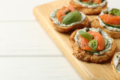 Tasty canapes with salmon, capers, cucumber and sauce on white wooden table, closeup. Space for text