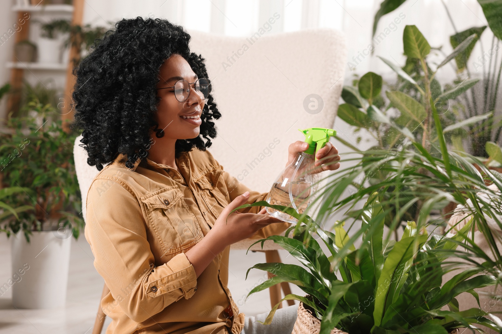 Photo of Happy woman spraying beautiful houseplant leaves with water indoors