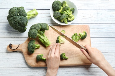 Photo of Woman cutting fresh green broccoli with knife on white wooden table, top view