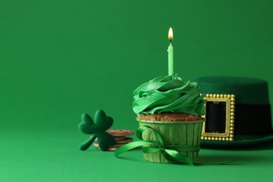 St. Patrick's day party. Tasty cupcake with burning candle and leprechaun hat on green background