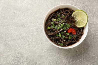 Photo of Tasty buckwheat noodles (soba) with sauce, onion and lime in bowl on light grey table, top view. Space for text