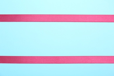 Photo of Simple pink ribbons on color background, top view