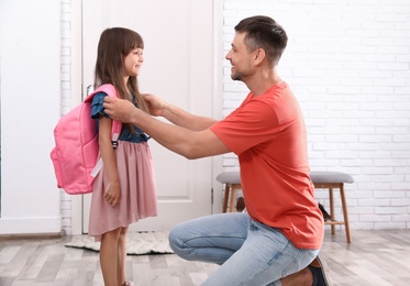 Photo of Happy father helping his little child to put on school bag at home