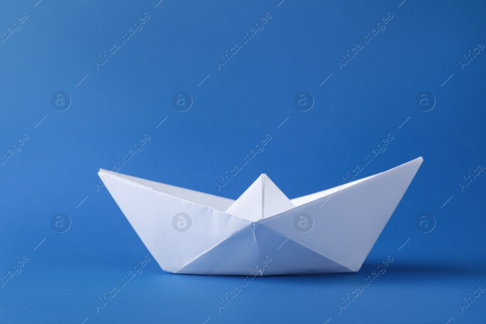 Photo of Handmade white paper boat on blue background. Origami art