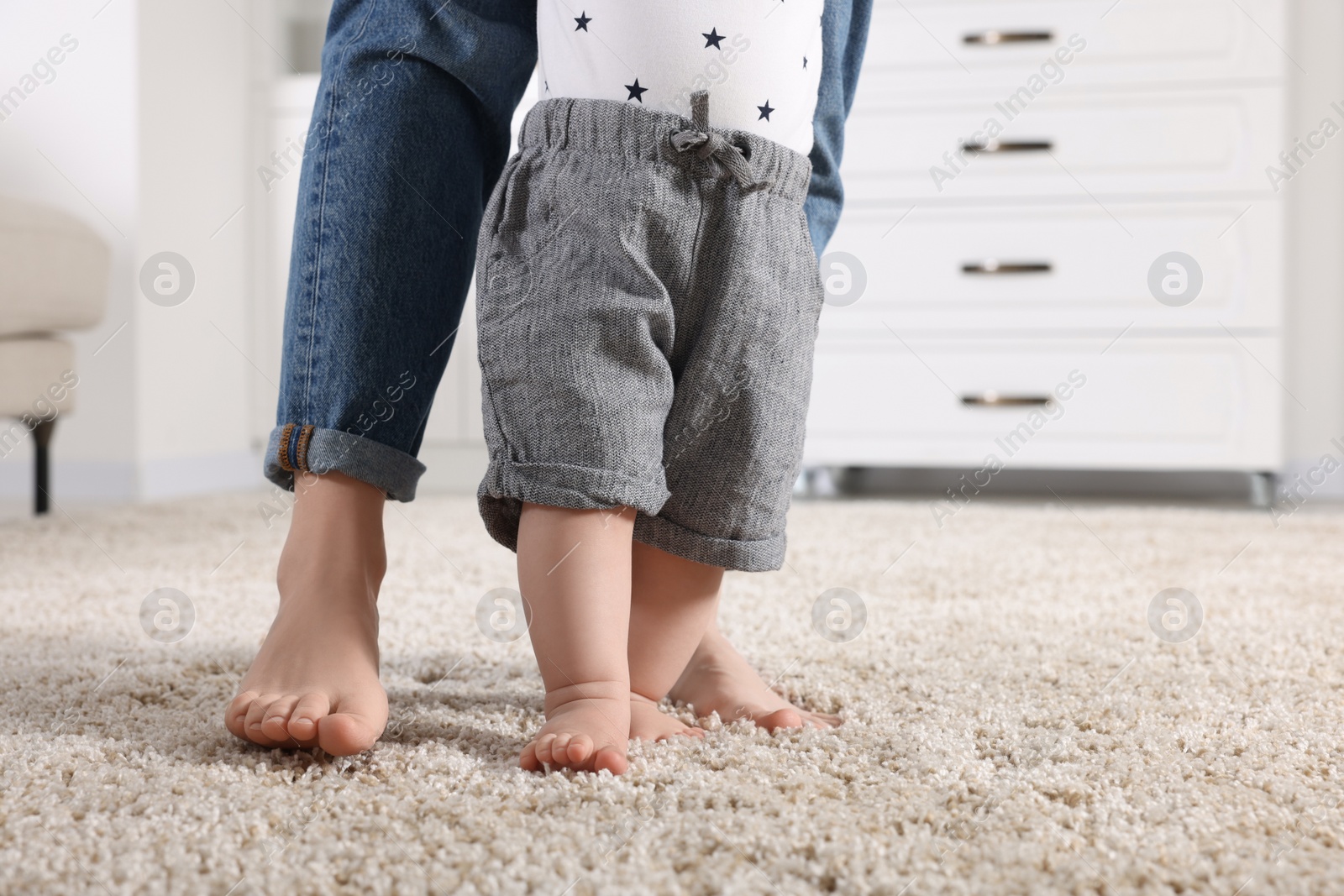 Photo of Mother supporting her baby son while he learning to walk on carpet at home, closeup. Space for text