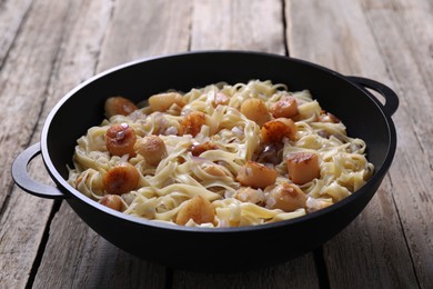 Delicious scallop pasta with onion in pan on wooden table, closeup