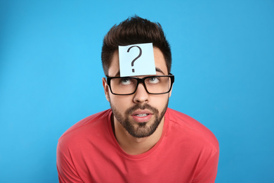 Emotional young man with question mark sticker on forehead against light blue background