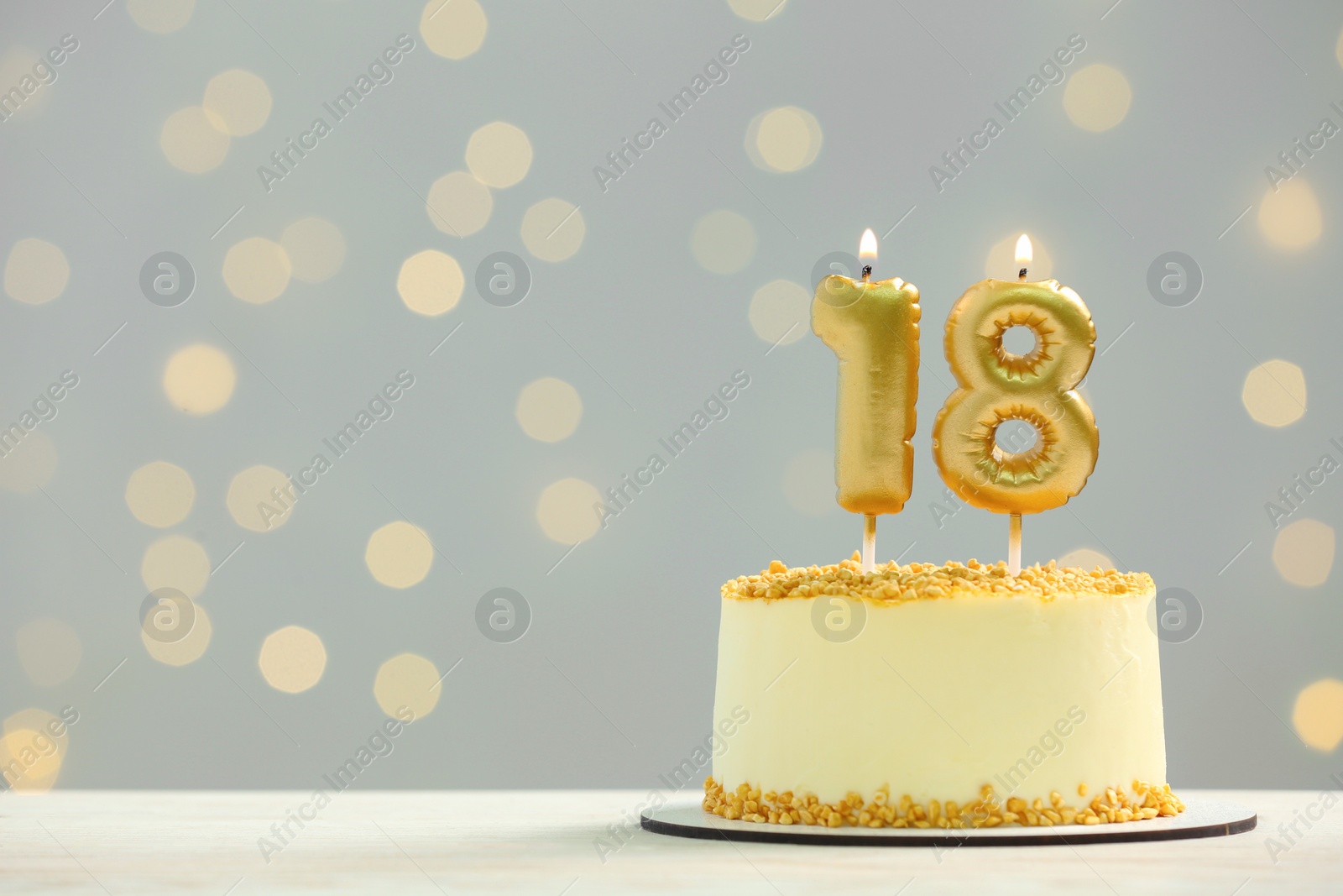 Photo of Coming of age party - 18th birthday. Delicious cake with number shaped candles on white table against blurred lights, space for text