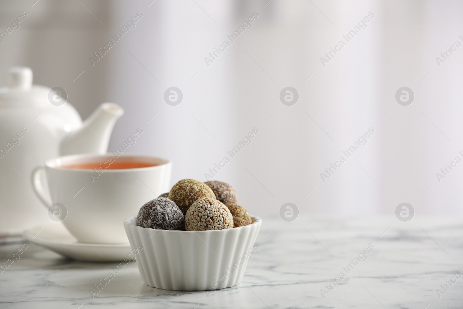 Photo of Different delicious vegan candy balls and tea on white marble table indoors. Space for text