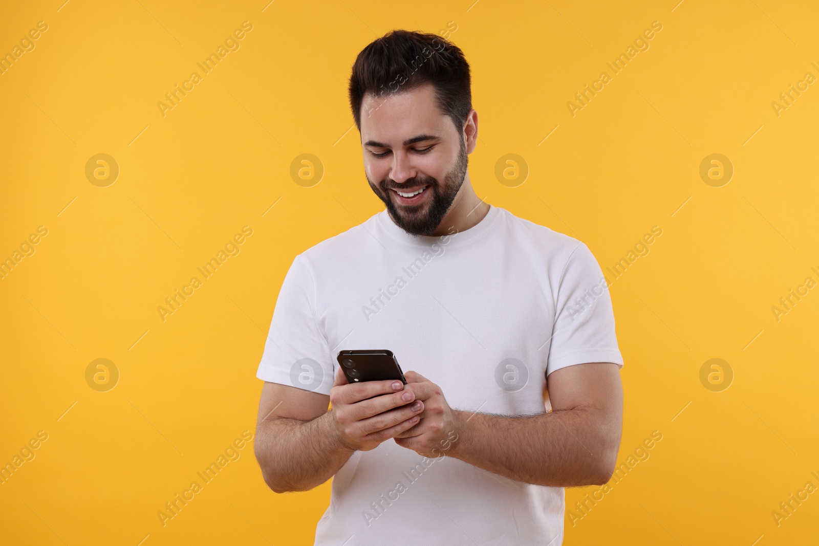 Photo of Happy young man using smartphone on yellow background