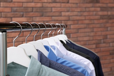 Wardrobe rack with stylish clothes near brick wall, closeup. Space for text