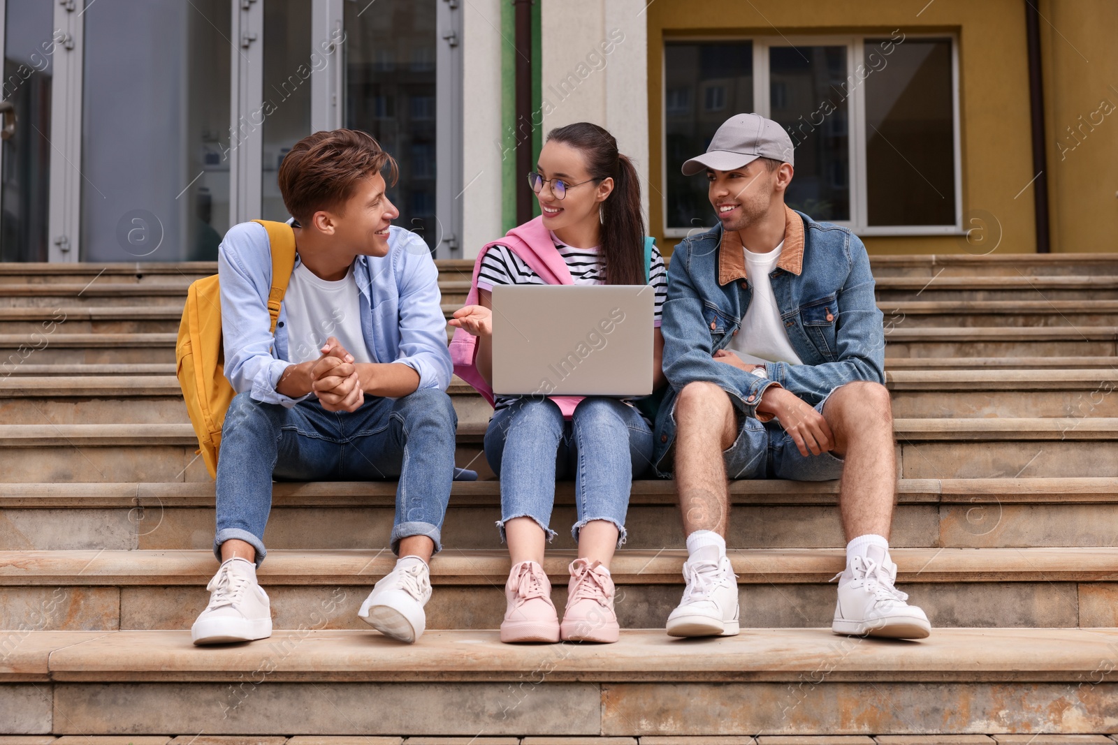 Photo of Happy young students studying together with laptop on steps outdoors