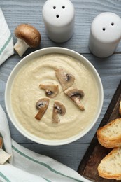 Photo of Delicious mushroom cream soup and ingredients on light grey wooden table, flat lay