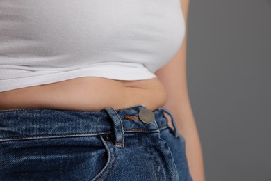Photo of Overweight woman in tight shirt and jeans on grey background, closeup. Space for text