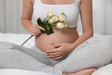 Pregnant woman with roses sitting on bed indoors, closeup