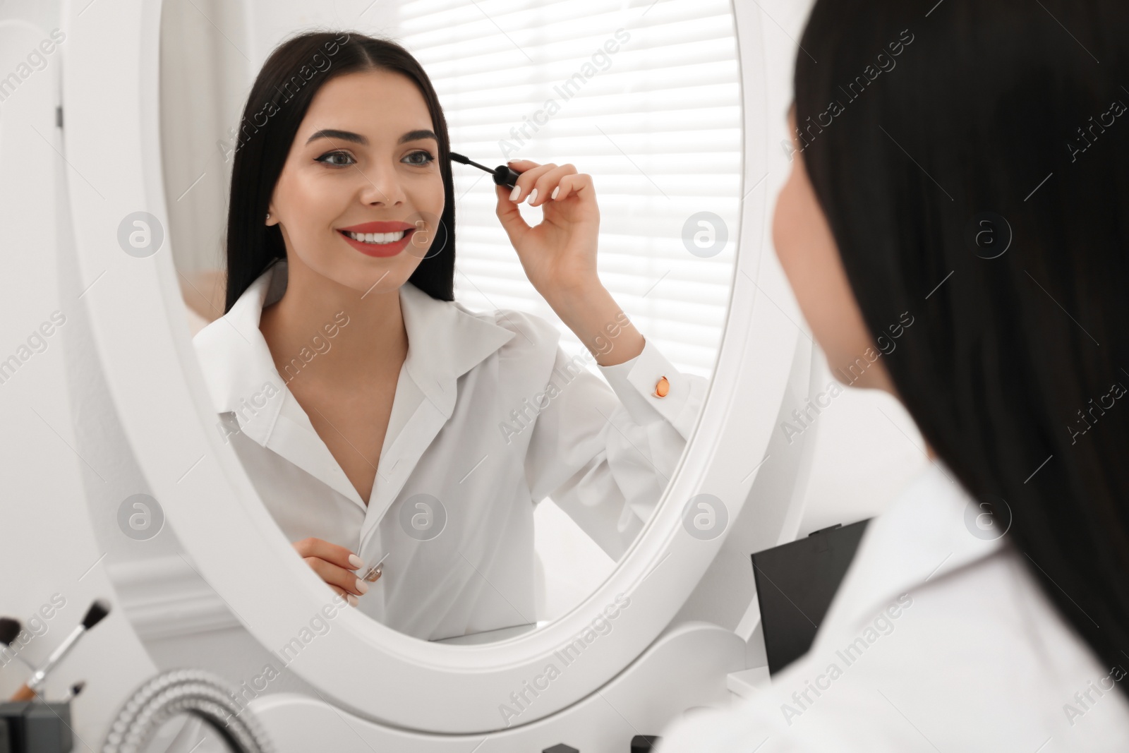 Photo of Beautiful woman applying makeup near mirror in room