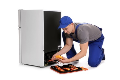 Photo of Male technician in uniform repairing refrigerator on white background