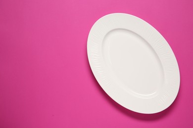 Photo of One white plate on pink background, top view. Space for text