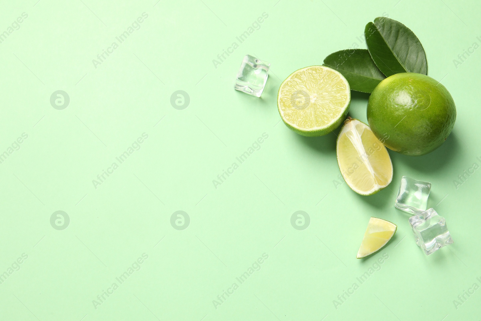 Photo of Fresh ripe limes with leaves and ice cubes on light green background, flat lay