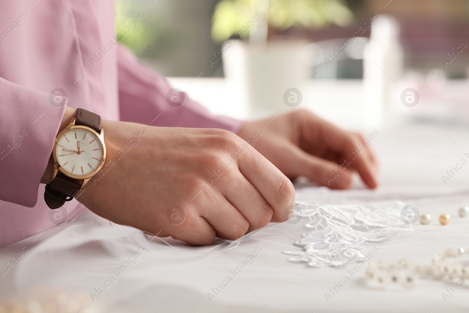 Photo of Dressmaker working with beautiful white lace at table in atelier, closeup