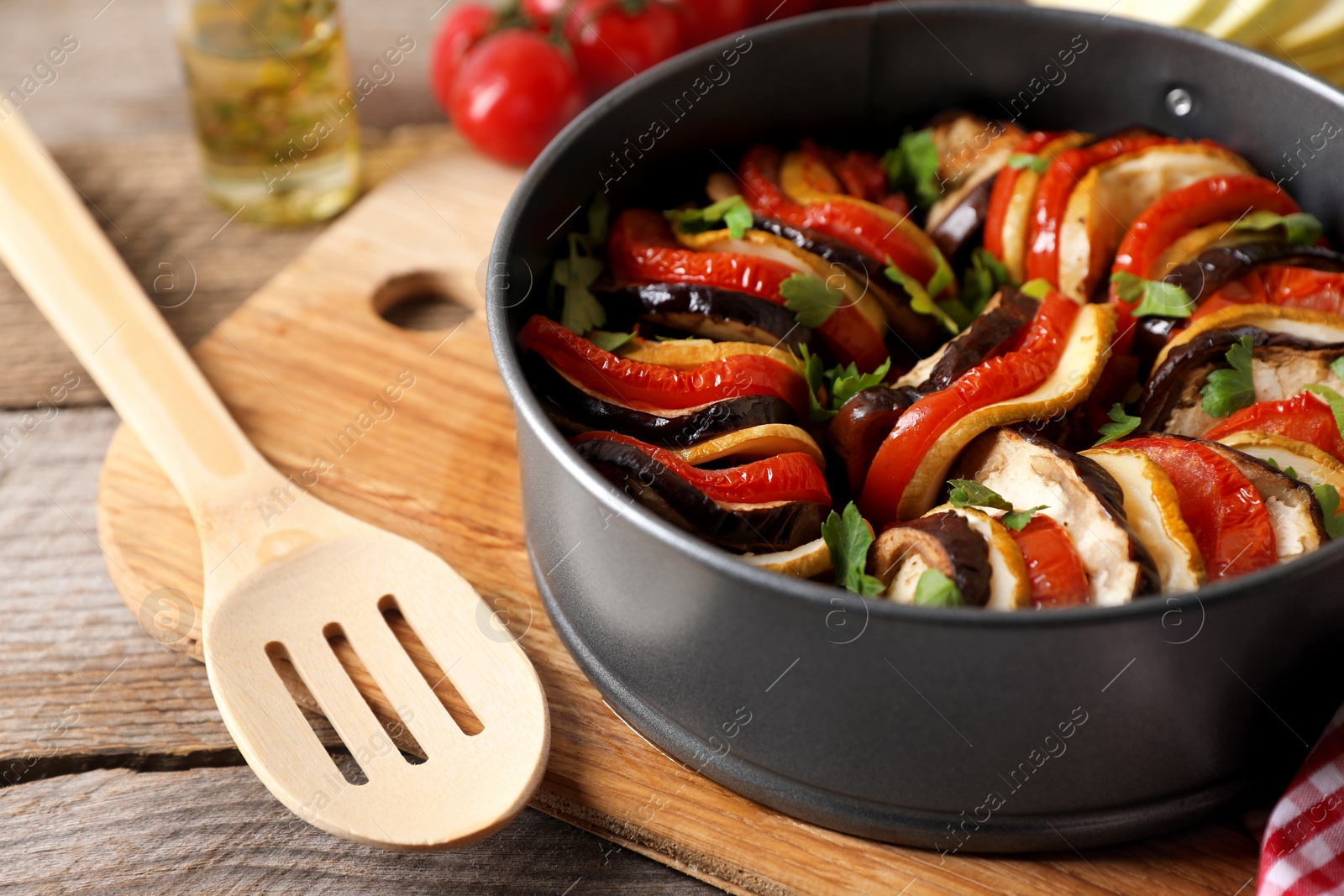 Photo of Delicious ratatouille in round baking pan and spatula on table, closeup