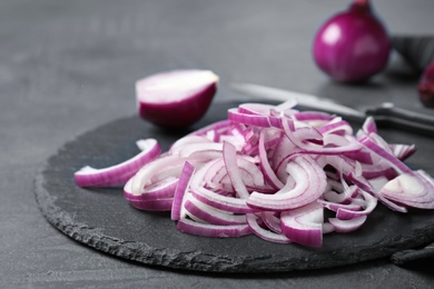 Photo of Slate plate with cut fresh red onion on table, closeup