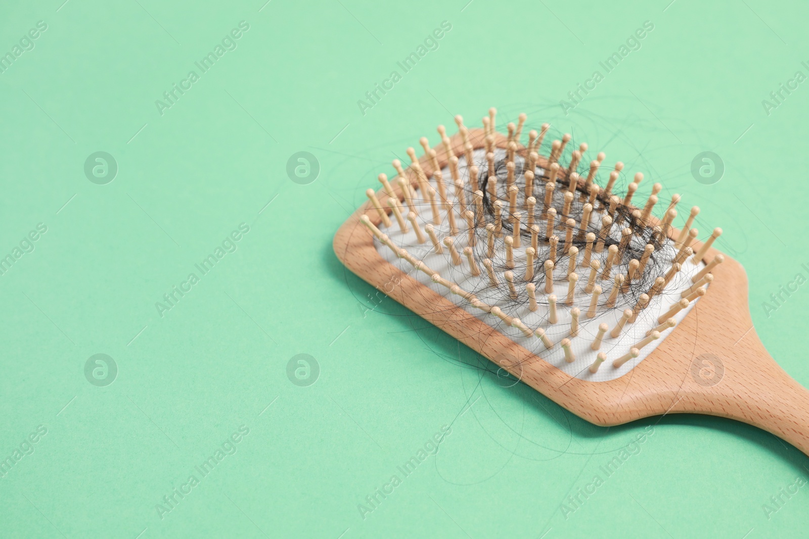 Photo of Wooden brush with lost hair on green background, closeup. Space for text