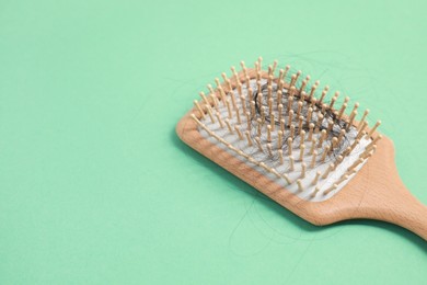 Photo of Wooden brush with lost hair on green background, closeup. Space for text