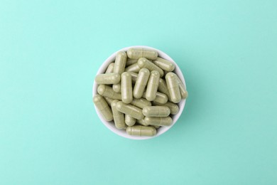 Photo of Vitamin capsules in bowl on turquoise background, top view