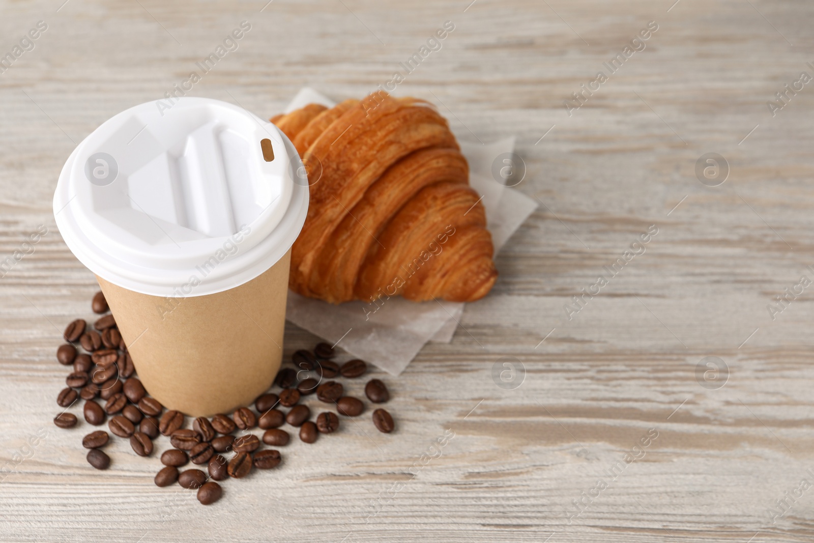 Photo of Coffee to go. Paper cup with tasty drink, croissant and beans on white wooden table. Space for text