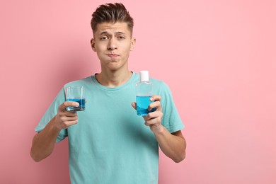 Young man using mouthwash on pink background, space for text