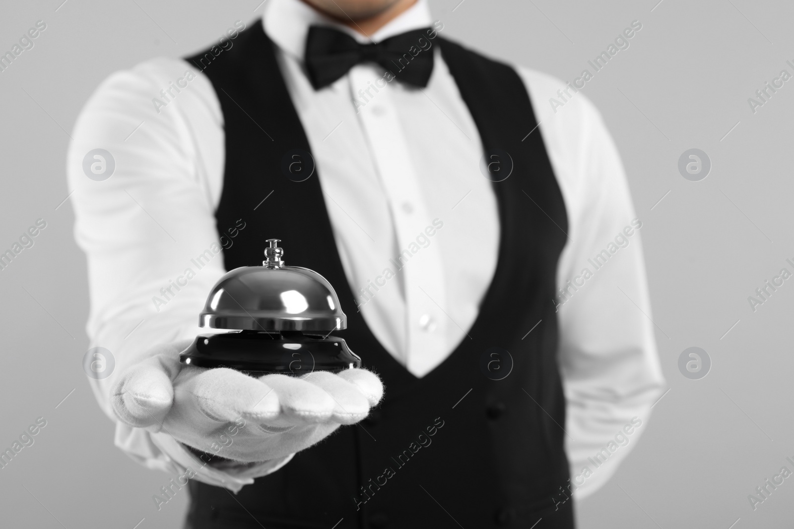 Photo of Butler holding service bell on grey background, closeup