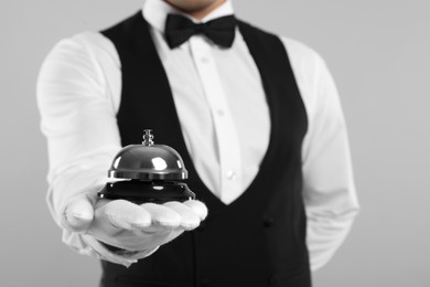 Butler holding service bell on grey background, closeup