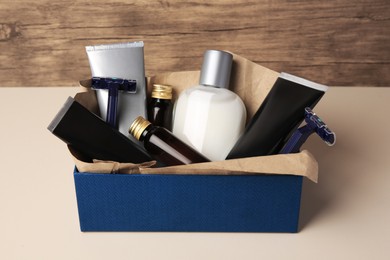 Box with different men's shaving accessories and cosmetics on beige table