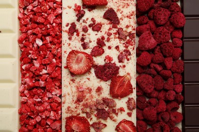 Photo of Chocolate bar with different freeze dried fruits as background, top view