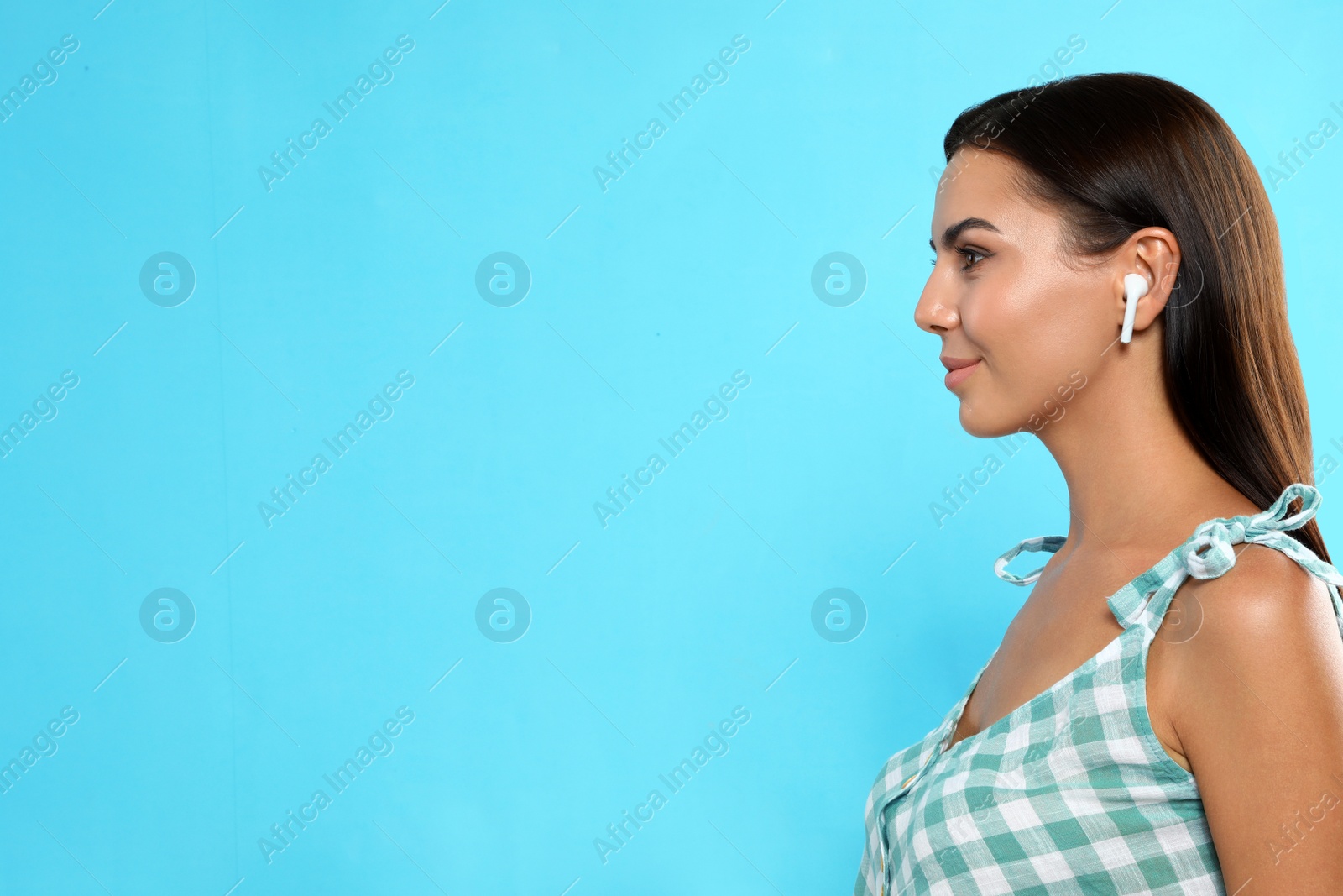 Photo of Young woman listening to music through wireless earphones on light blue background. Space for text