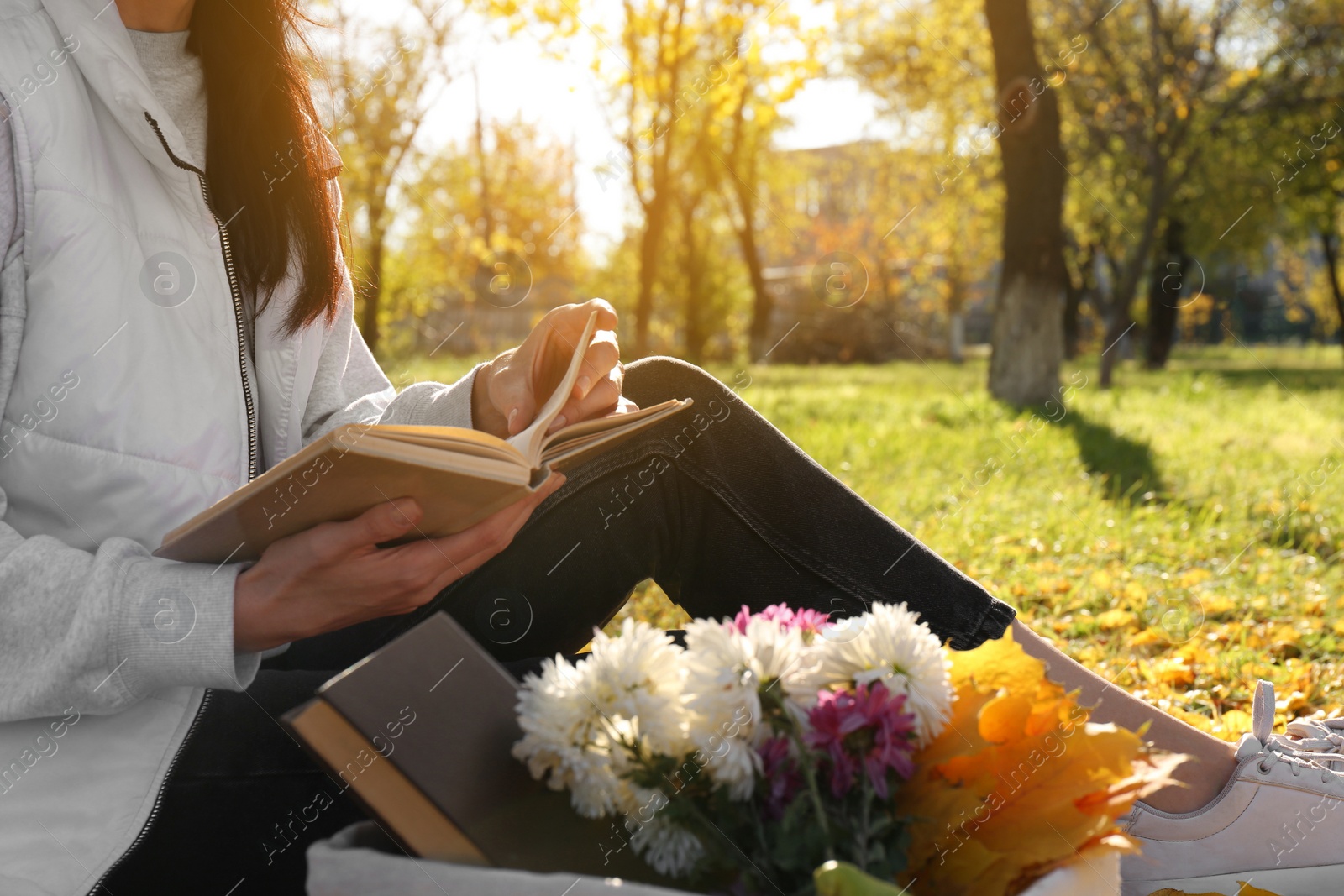 Photo of Woman reading book outdoors in park on autumn day, closeup