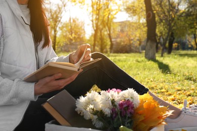 Woman reading book outdoors in park on autumn day, closeup